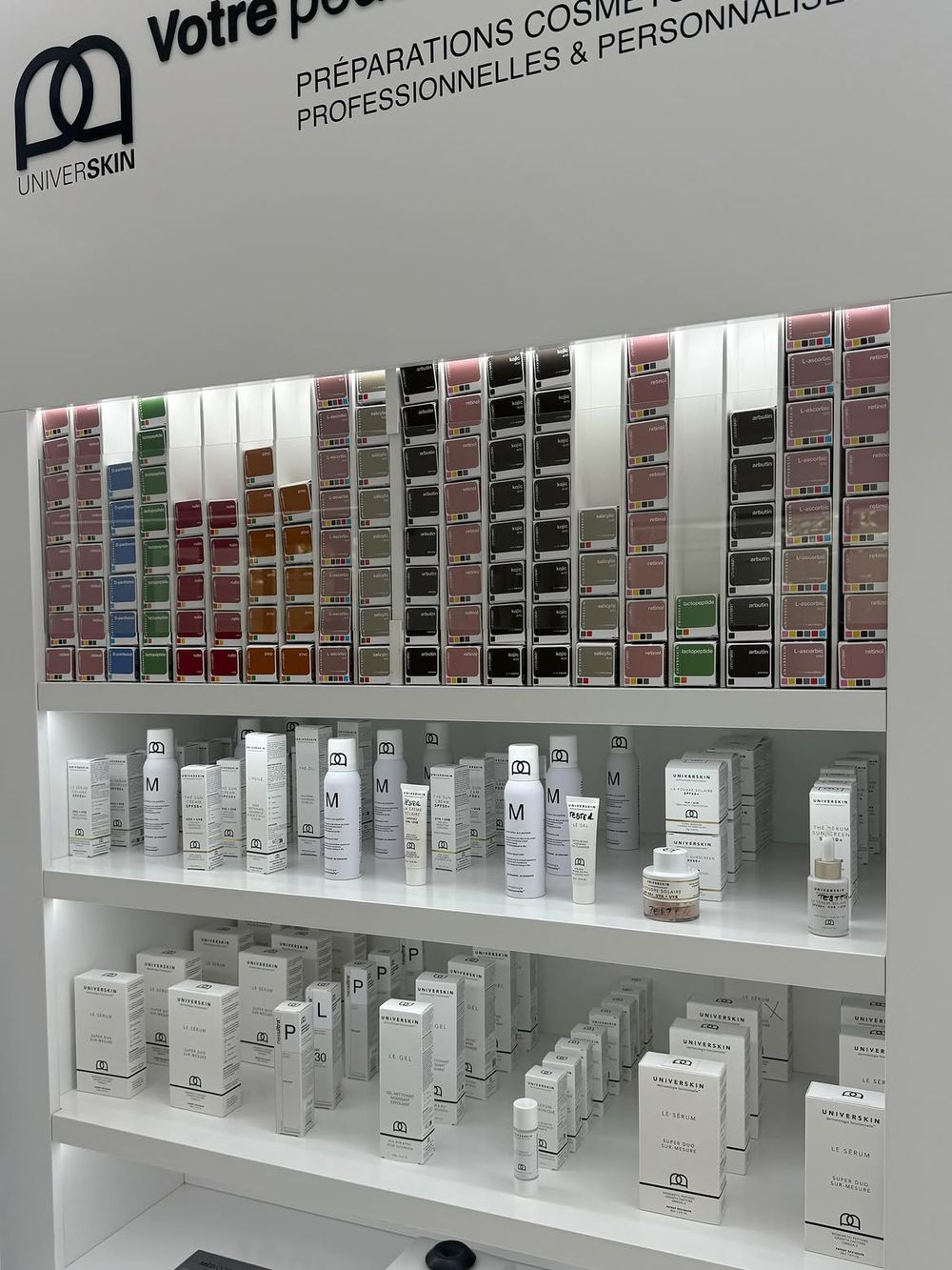 Un présentoir Universkin montrant la gamme d’ingrédients actifs classés par couleur au-dessus de la ligne de produits finis