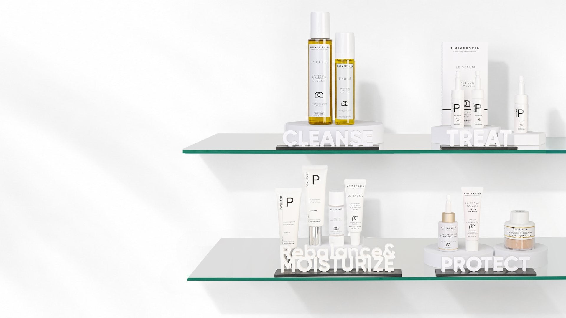 Dos estantes de cristal con la gama Universkin, agrupada en limpiar, tratar, reequilibrar e hidratar, y proteger